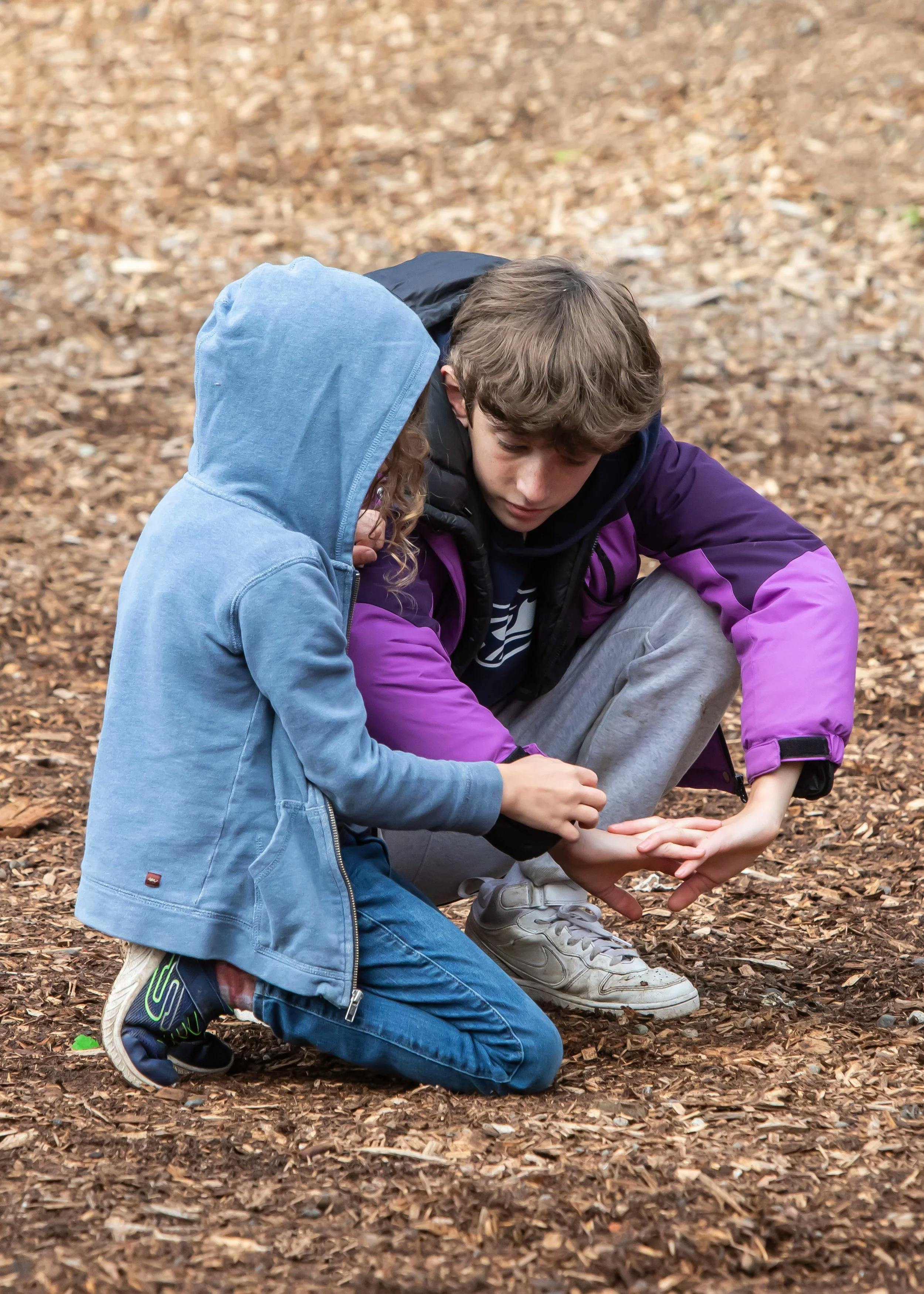 Two children crouching and looking at something on the ground