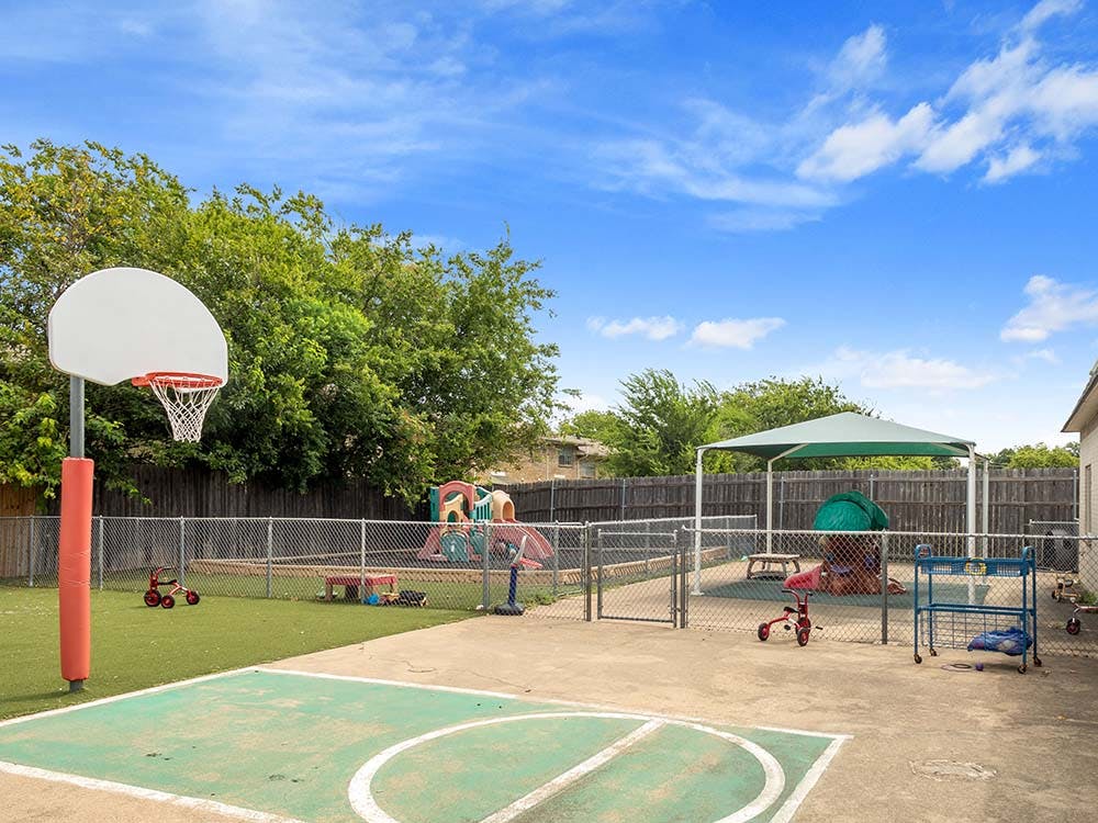 Outdoor playground area with a basketball hoop, sandpit, and play structure
