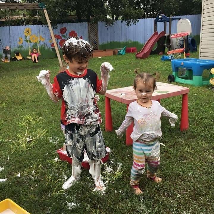 Two children covered in white foam in a grassy yard