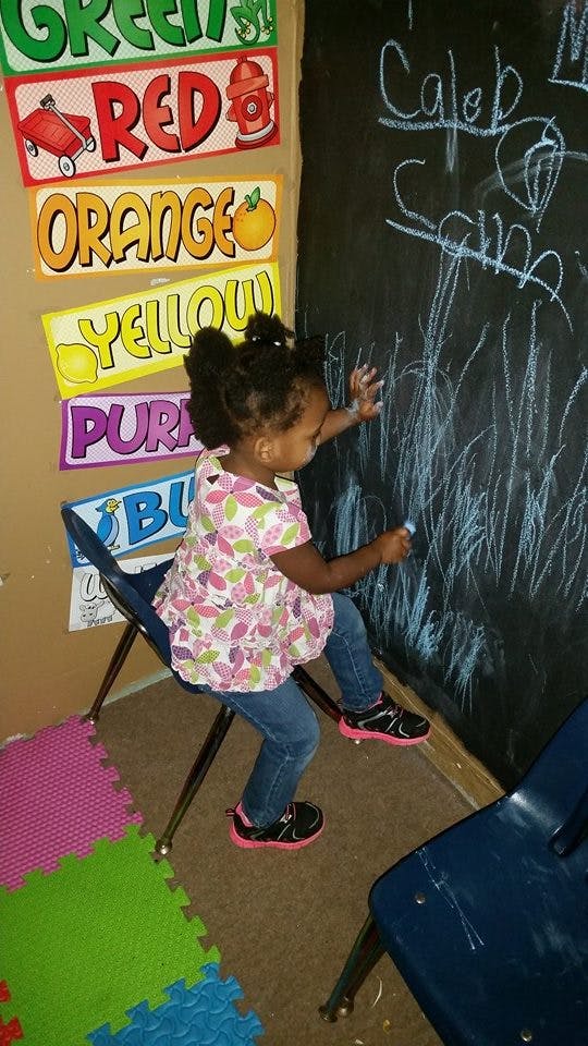 Child sitting on a chair and drawing on a chalkboard