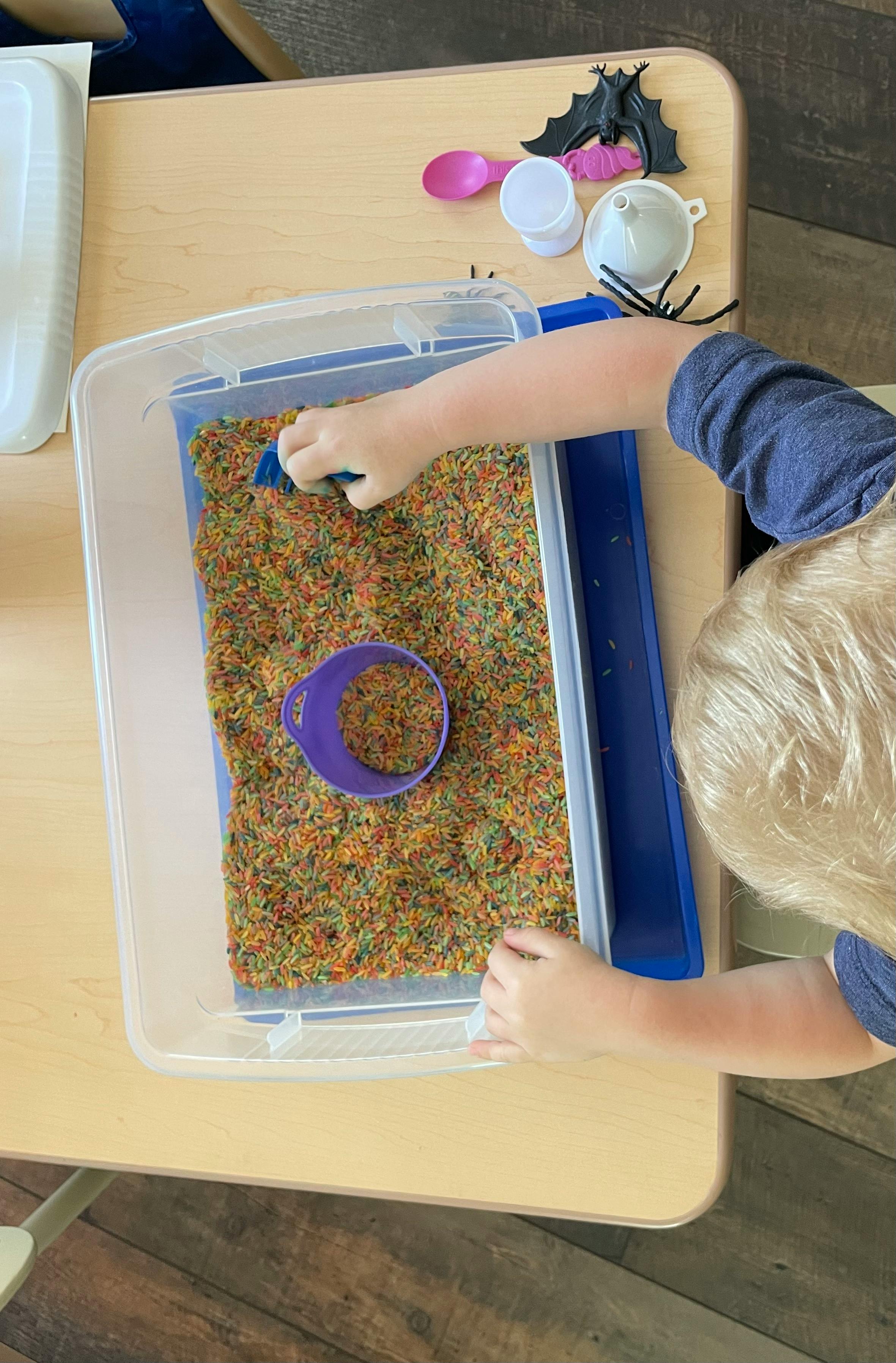 Child playing with colorful rice in a sensory bin