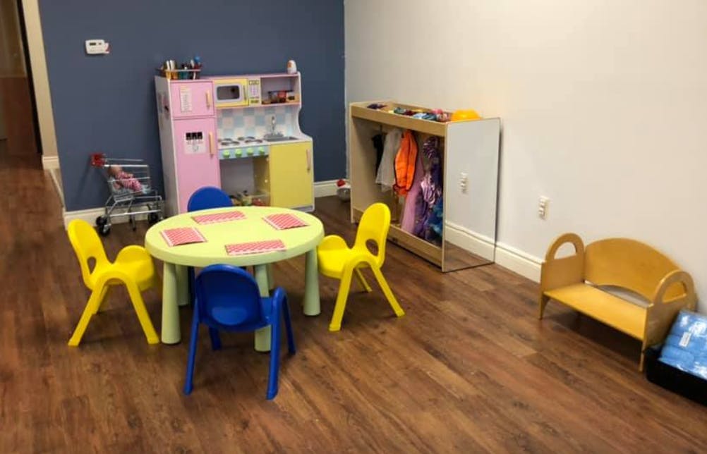 Children's play area with small table and chairs, toy kitchen, and dress-up rack