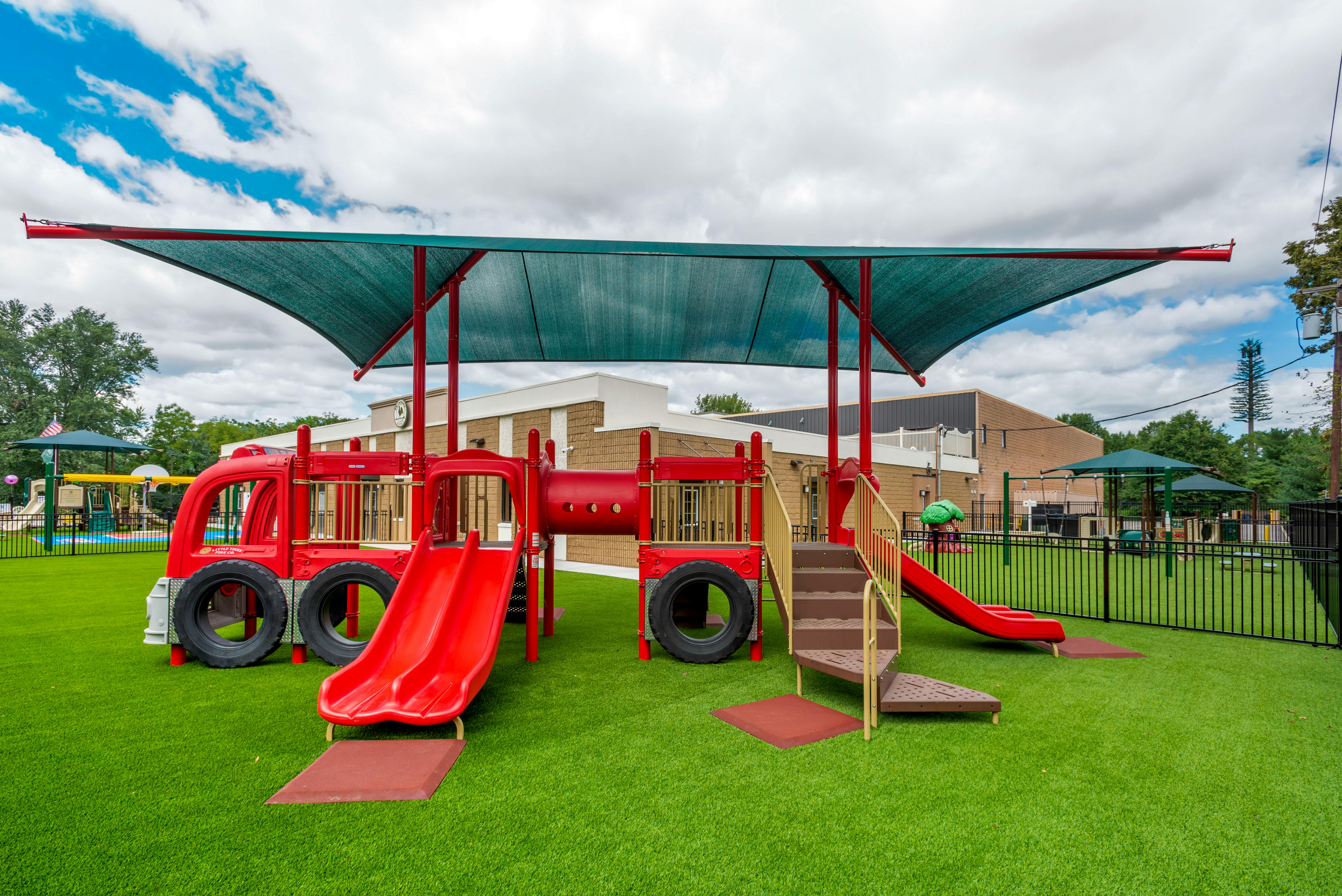 A red play structure with slides and climbing elements, covered by a green shade