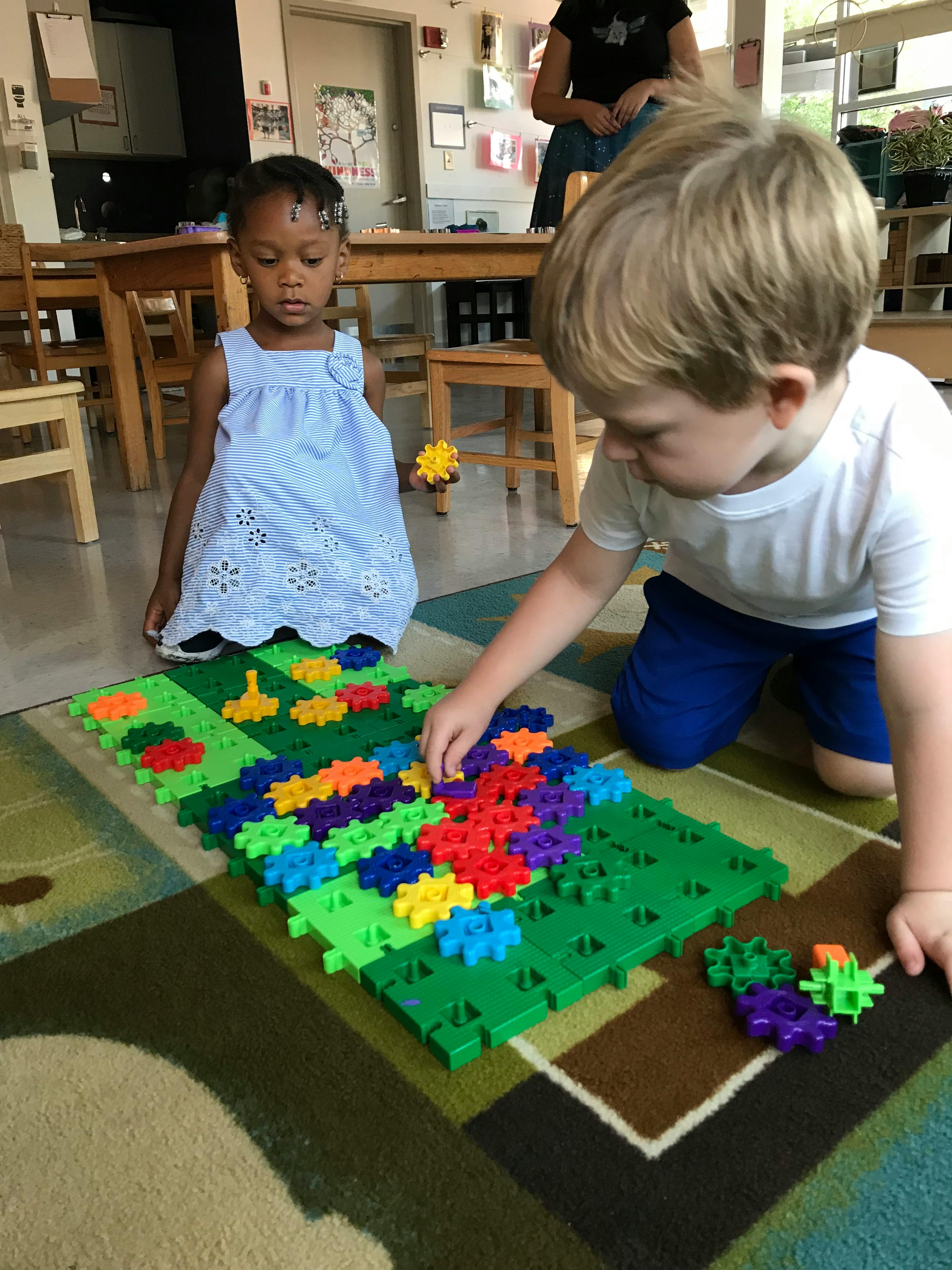 Two children playing with colorful interlocking gears on a green base