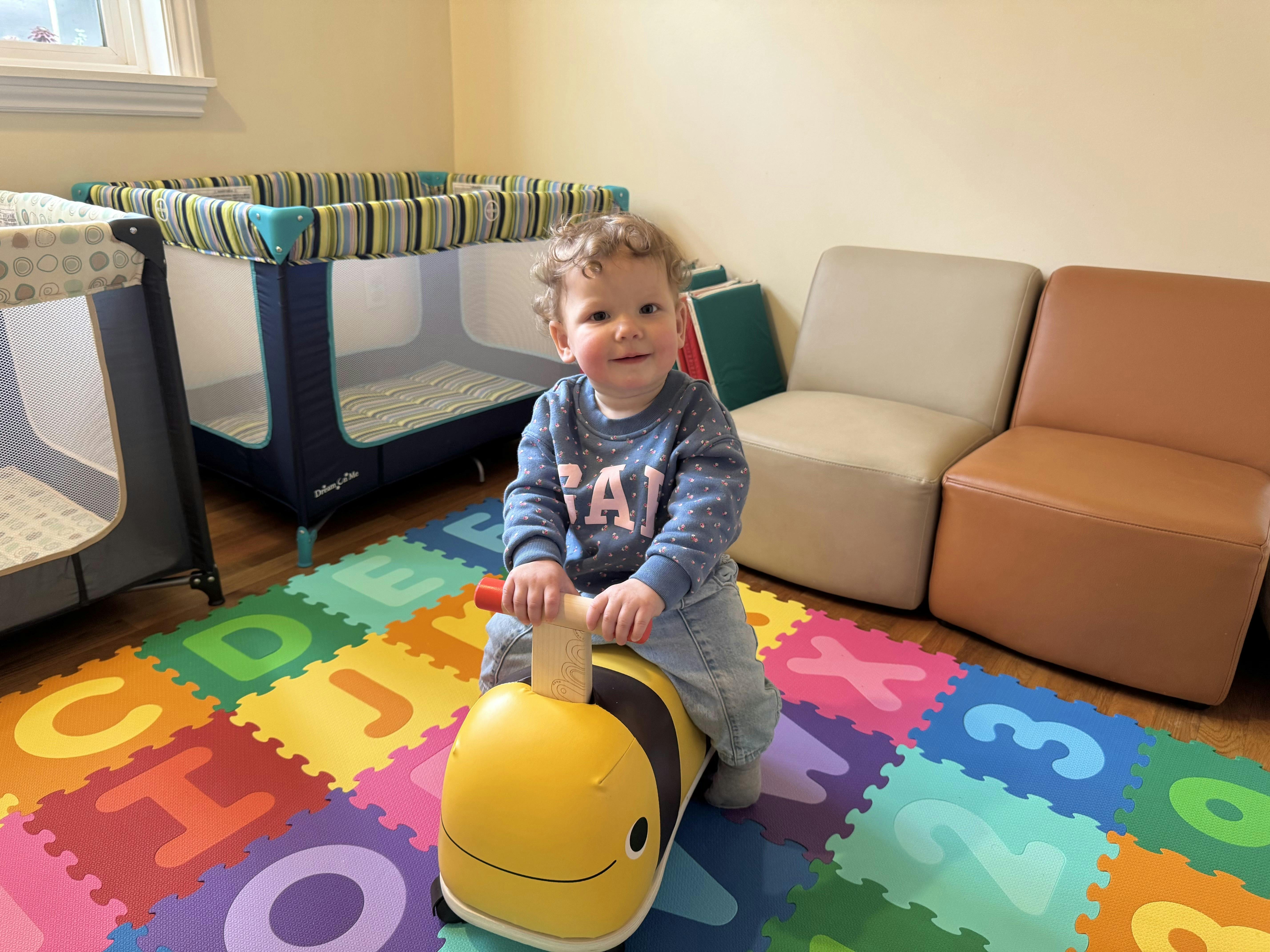 Child riding a bee-shaped toy on a colorful foam alphabet play mat