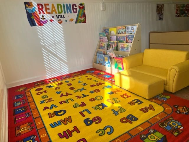 Children's reading nook with alphabet rug, yellow chair, and book display