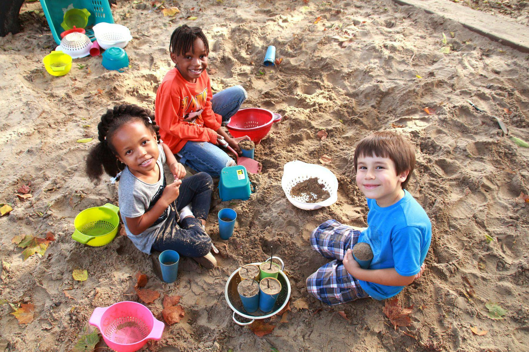 Three children playing in a sandbox with toys