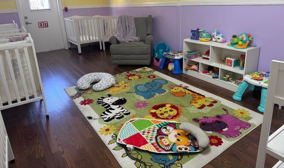 Cribs and an armchair in a childcare room with a colorful animal rug
