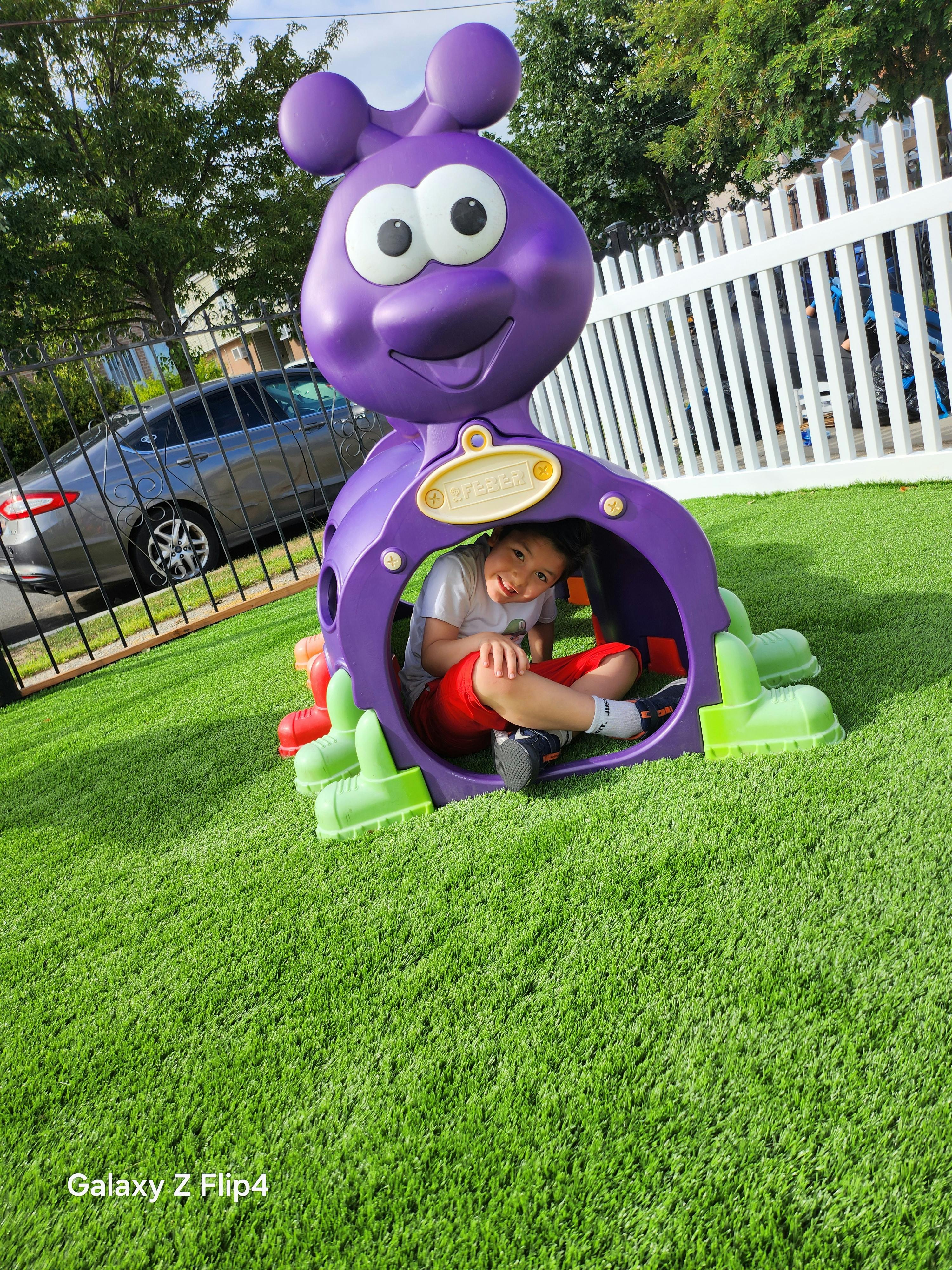 Child sitting inside a purple play structure on artificial grass