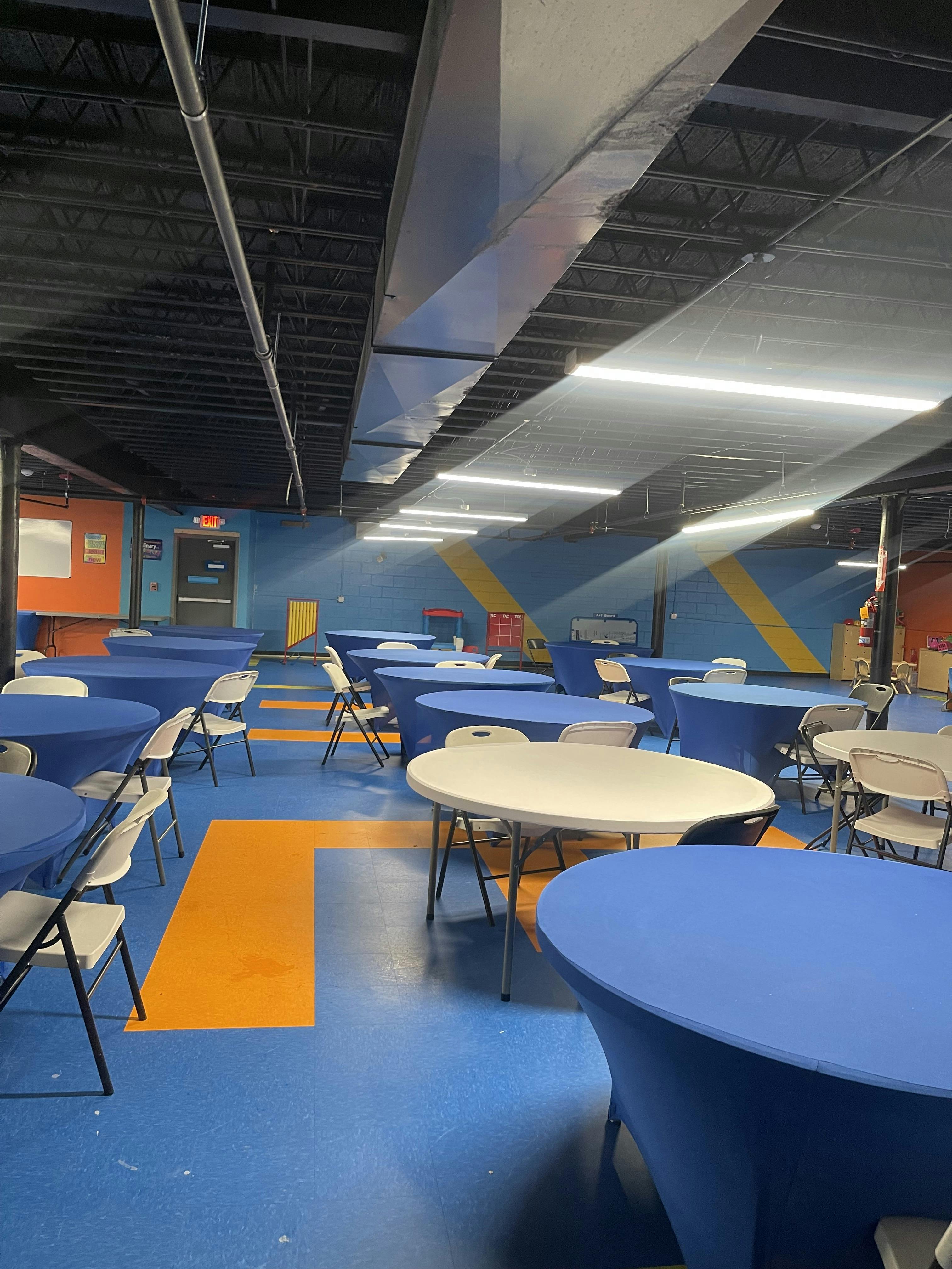A room with blue and orange flooring, multiple tables with blue tablecloths