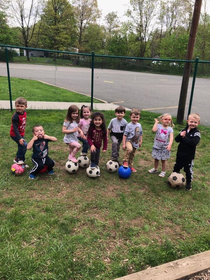 Group of children standing with soccer balls on a grassy field