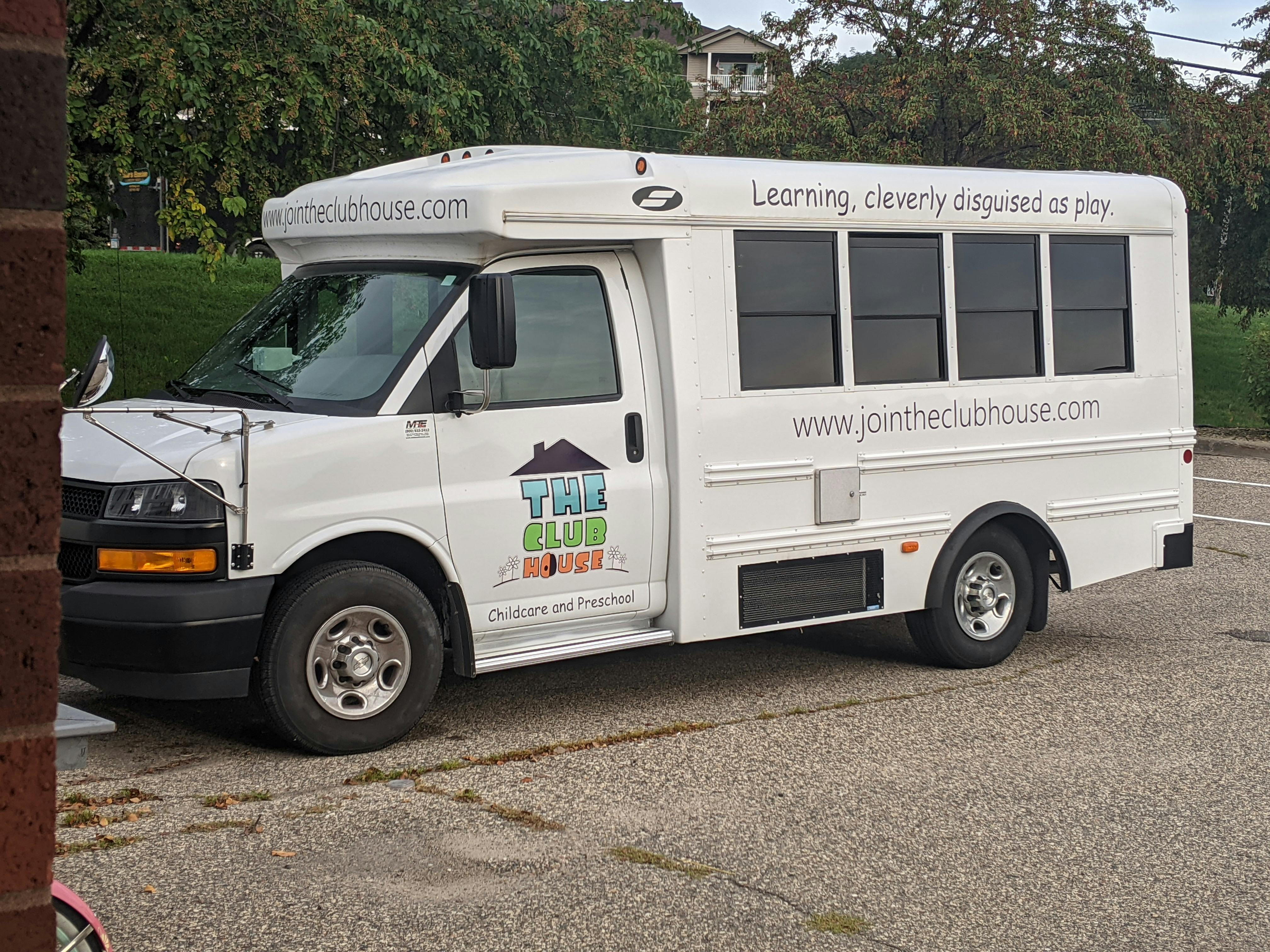 White shuttle bus with "The Club House" logo and text "Learning cleverly disguised as play"