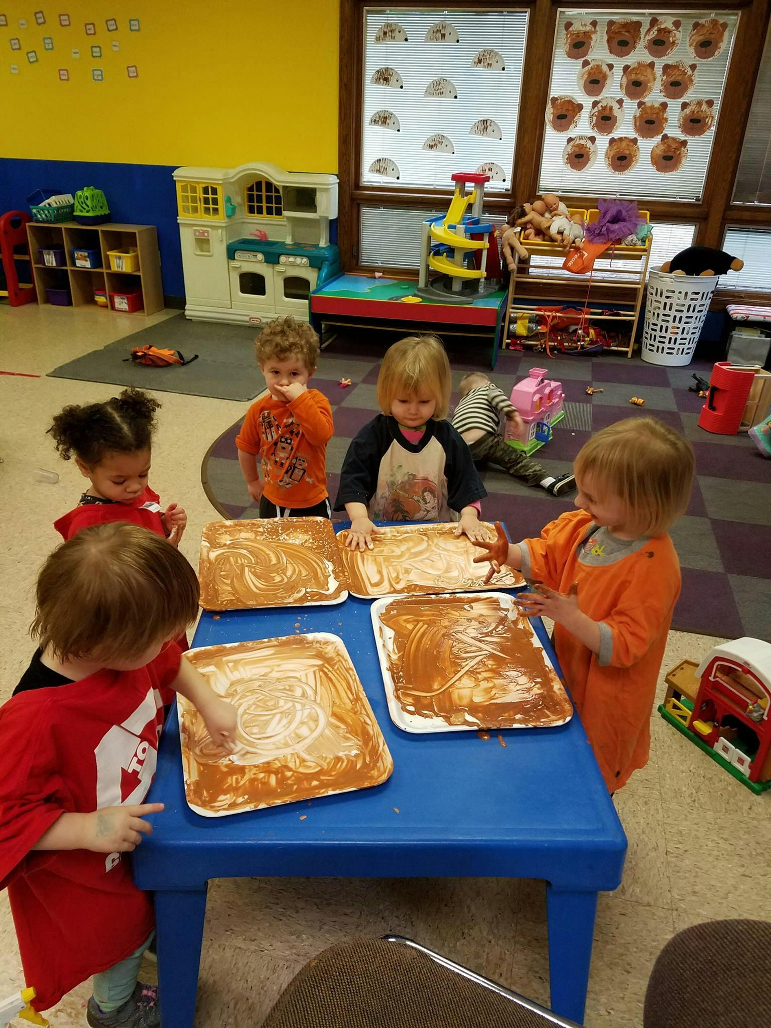 Children finger painting at a blue table in a classroom