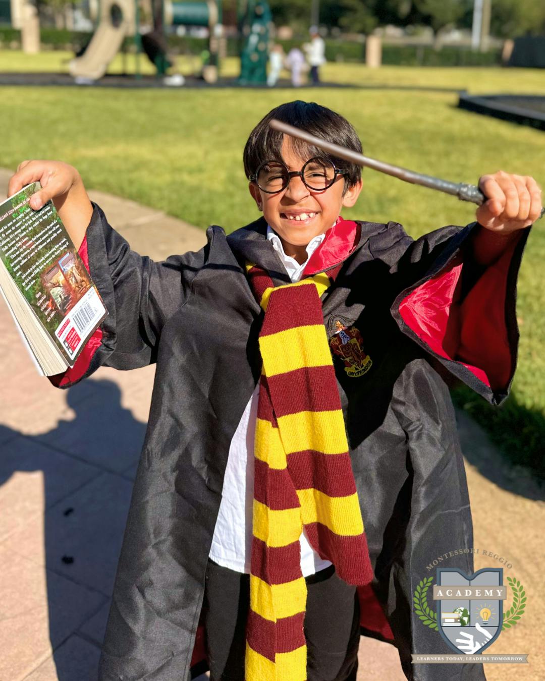 Child in glasses and robe holding a book and a wand