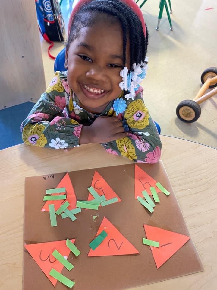 Child smiling at a table with paper triangles and green strips