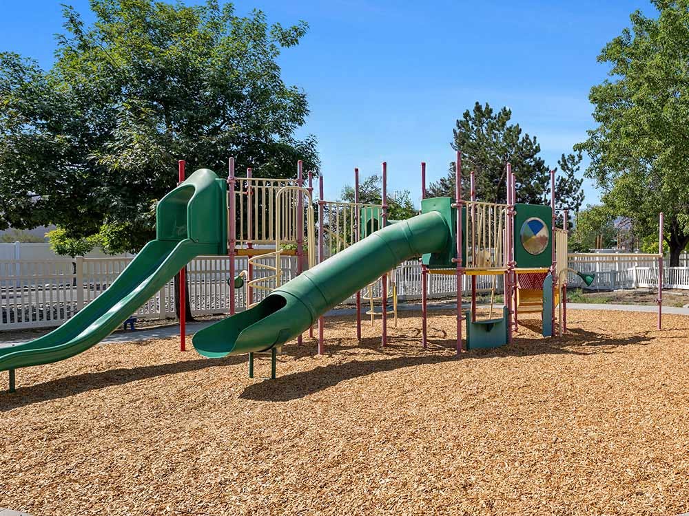 Empty children's playground with green slides and wood chip ground cover