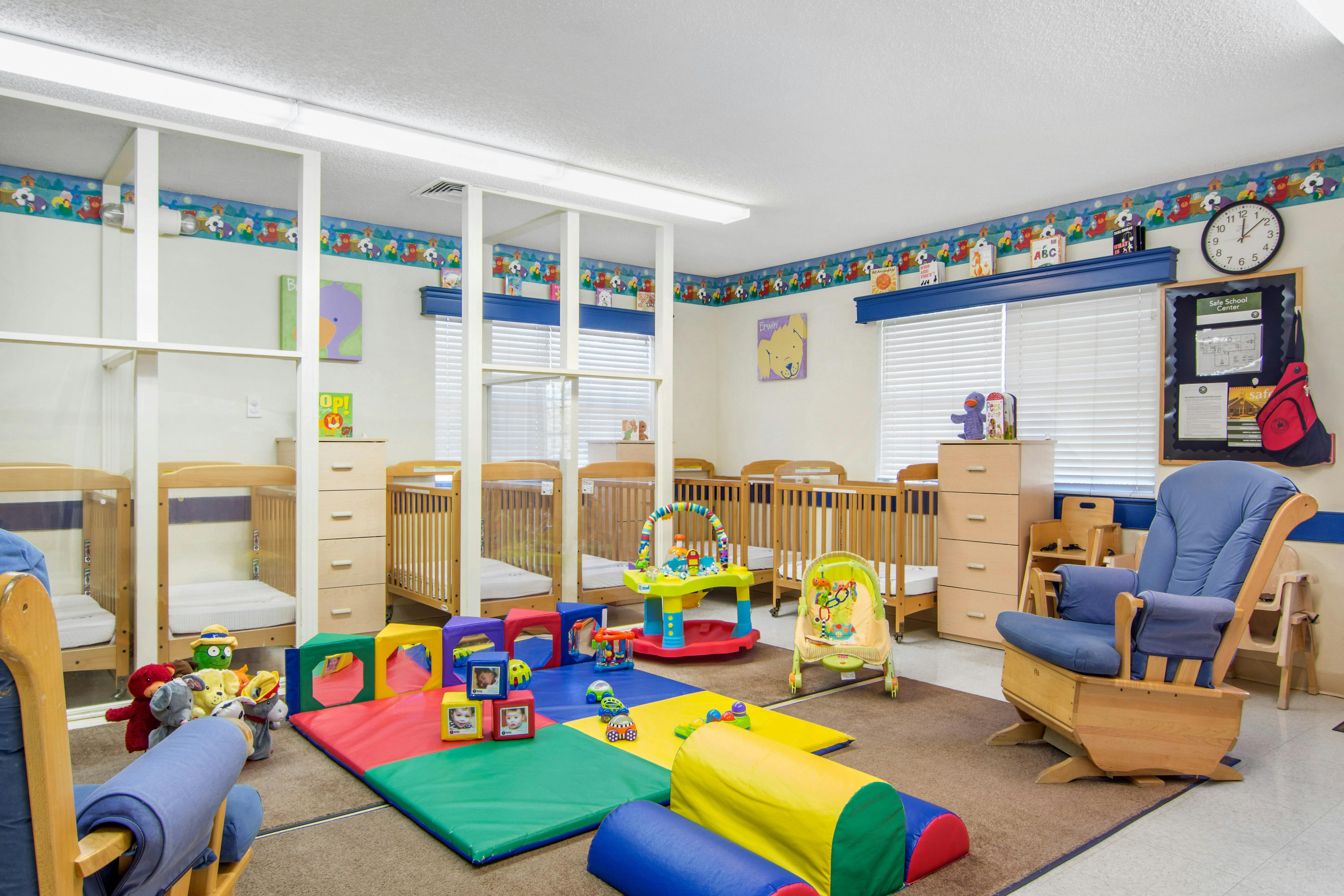 A colorful baby room with multiple cribs, a blue rocking chair, and play mats
