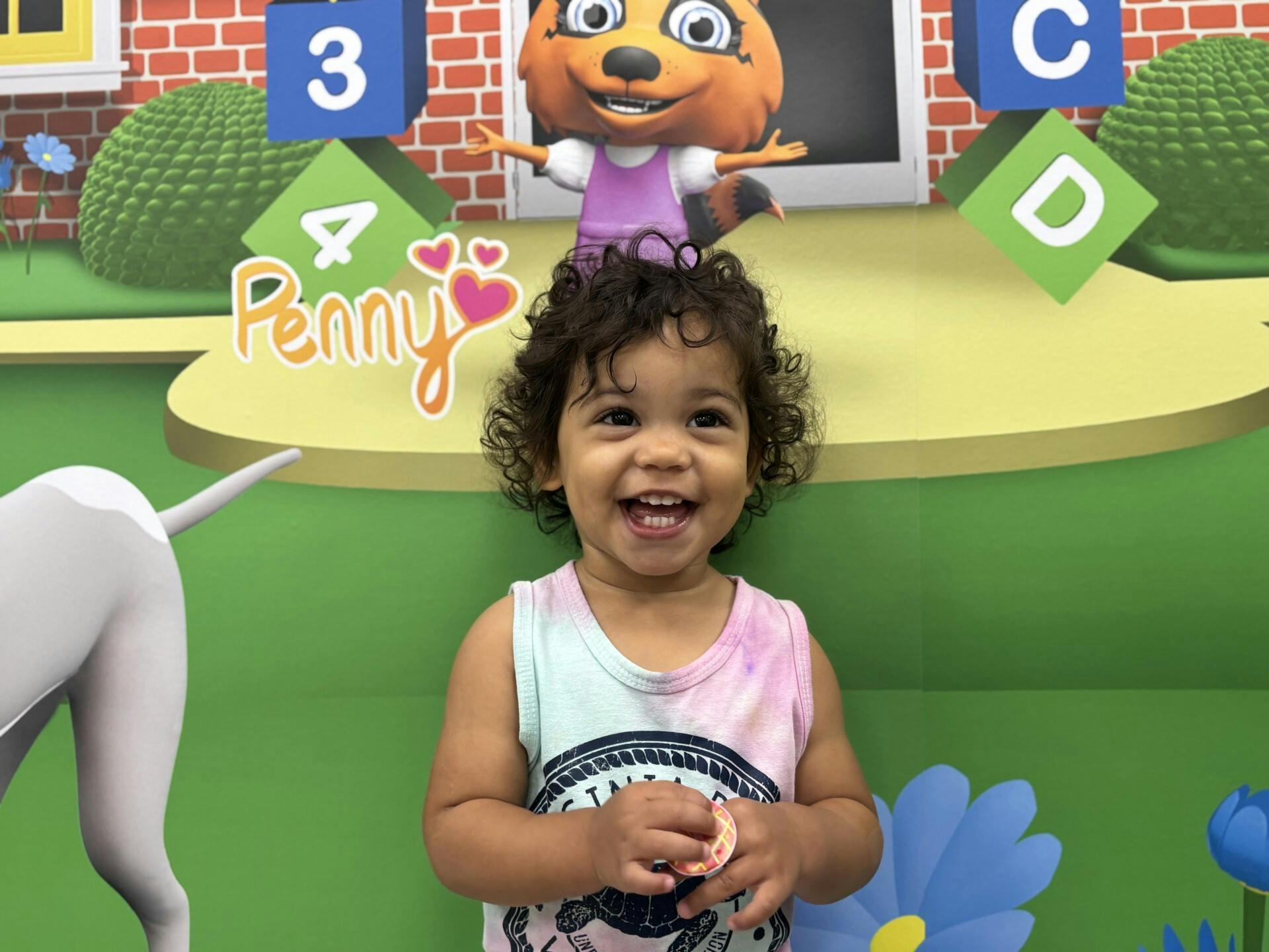 Child smiling in front of a colorful cartoon backdrop with the name Penny