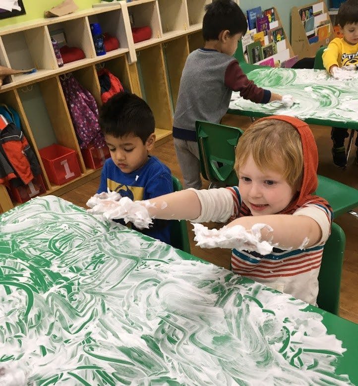 Children playing with shaving cream on a green table in a classroom