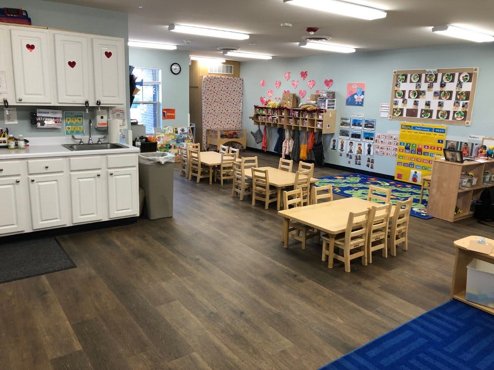 Classroom with small tables and chairs, cubbies, and a play kitchen area