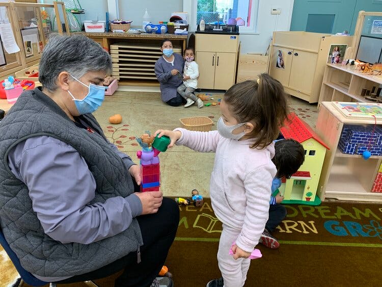 Person and child wearing masks playing with toys in a classroom