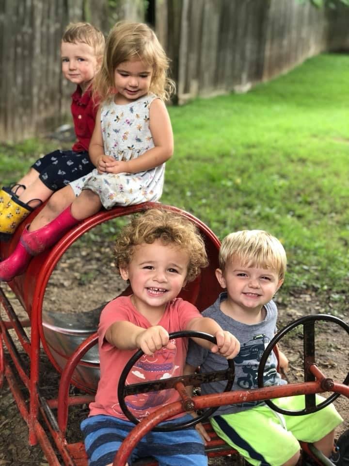 Three children and two toddlers playing on a red toy train