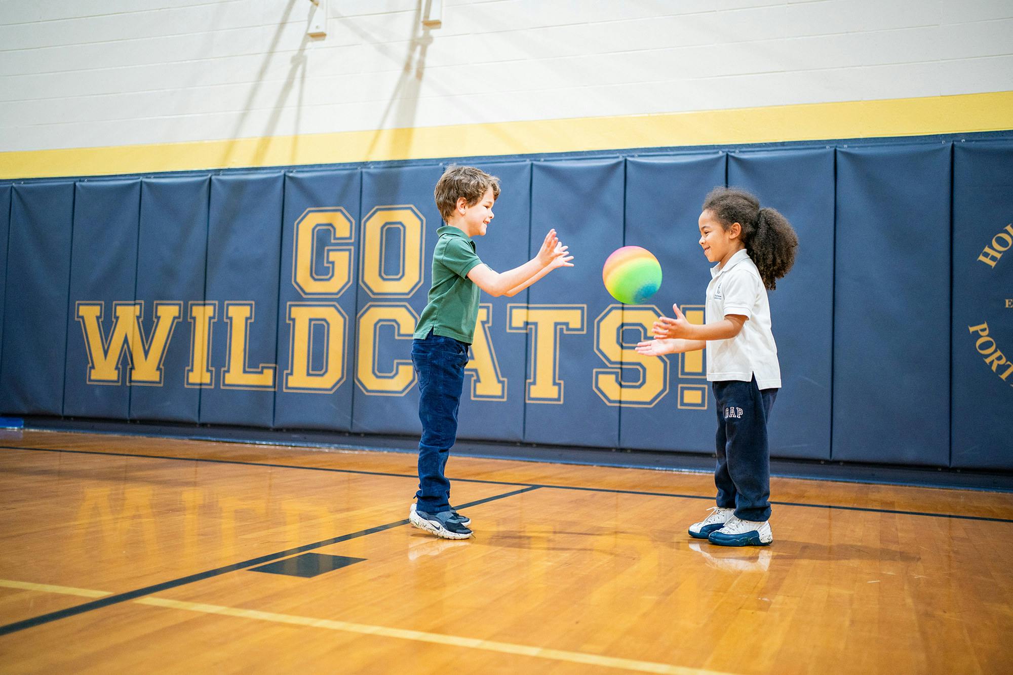 Two children playing with a colorful ball in a gymnasium