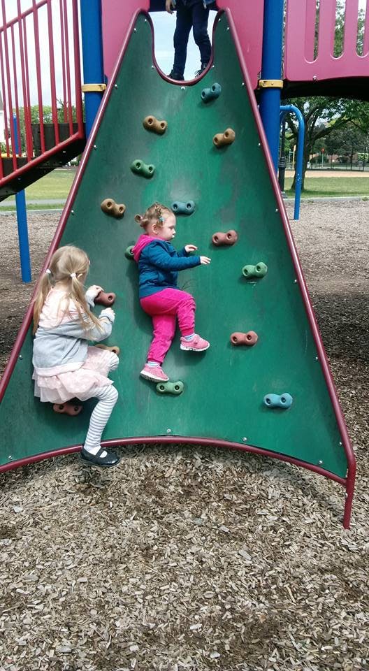 Two children climbing a rock wall on a playground