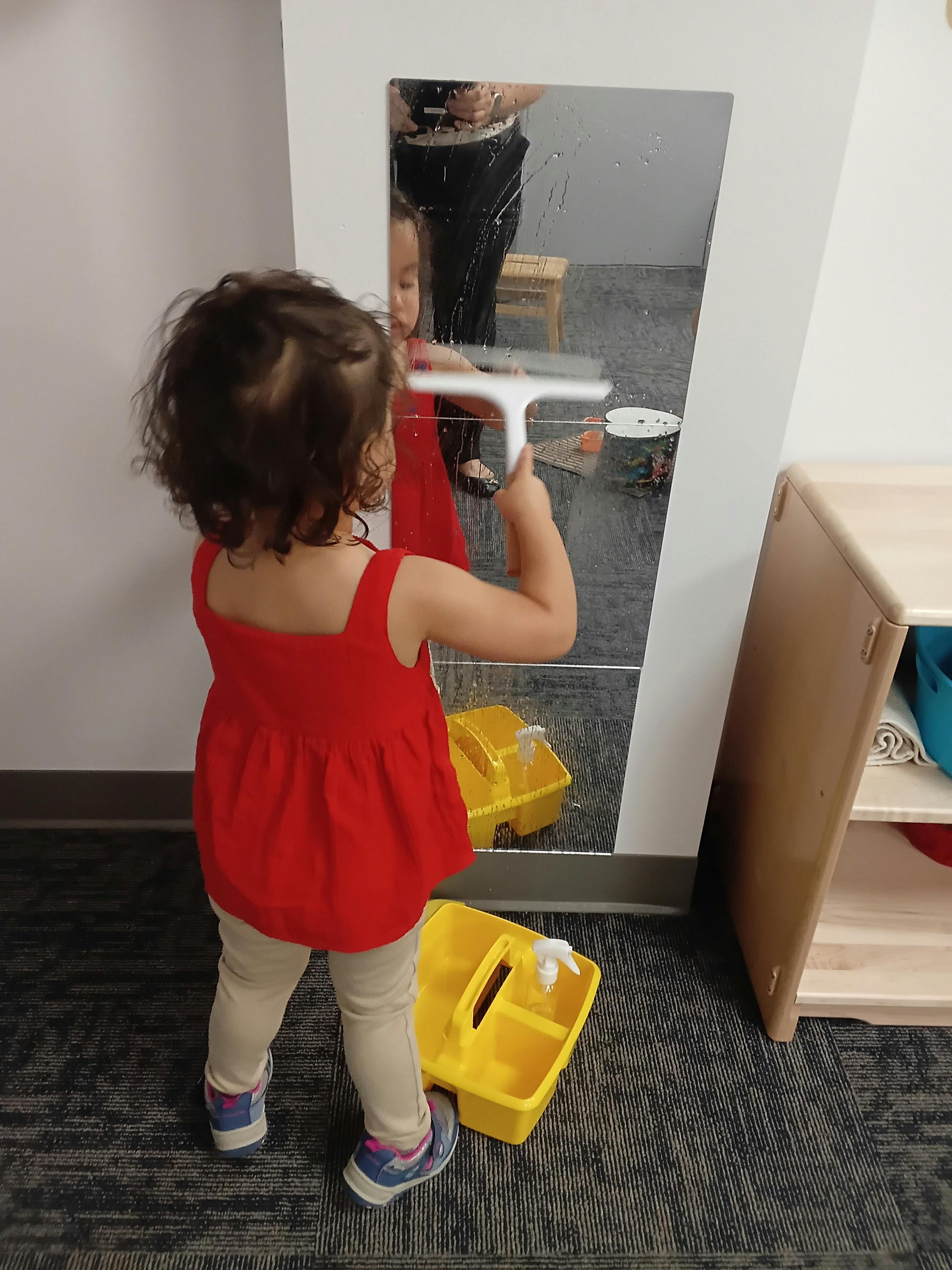 Child cleaning a mirror with a squeegee