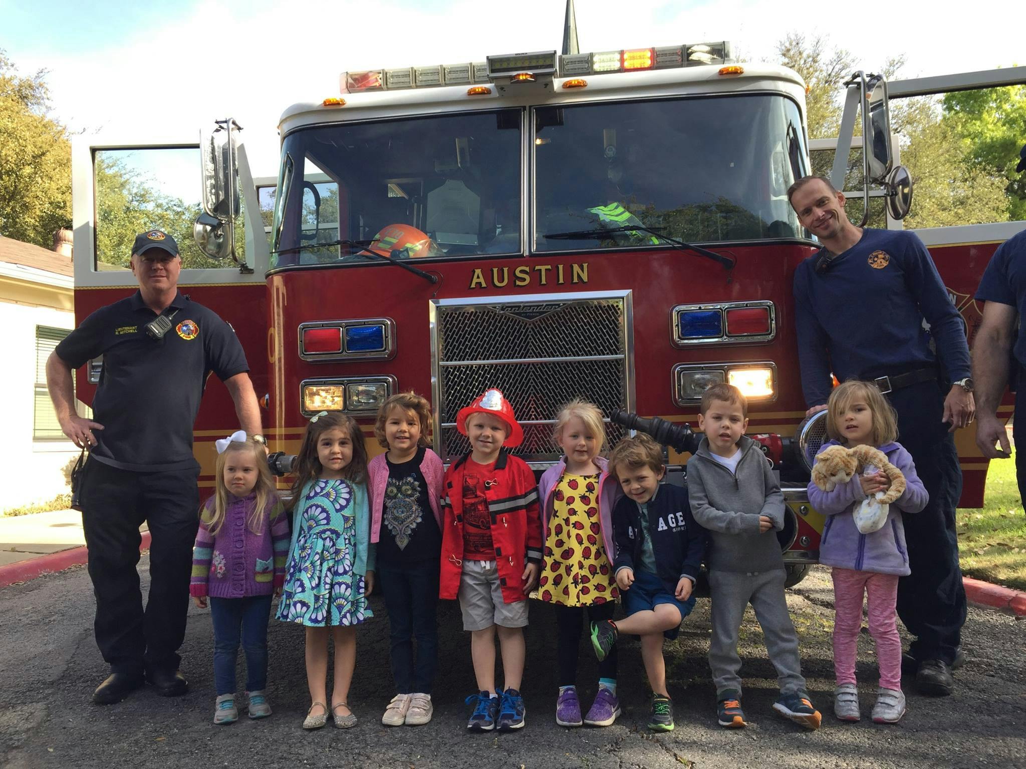 Two people and multiple children standing in front of a fire truck with "AUSTIN" on it