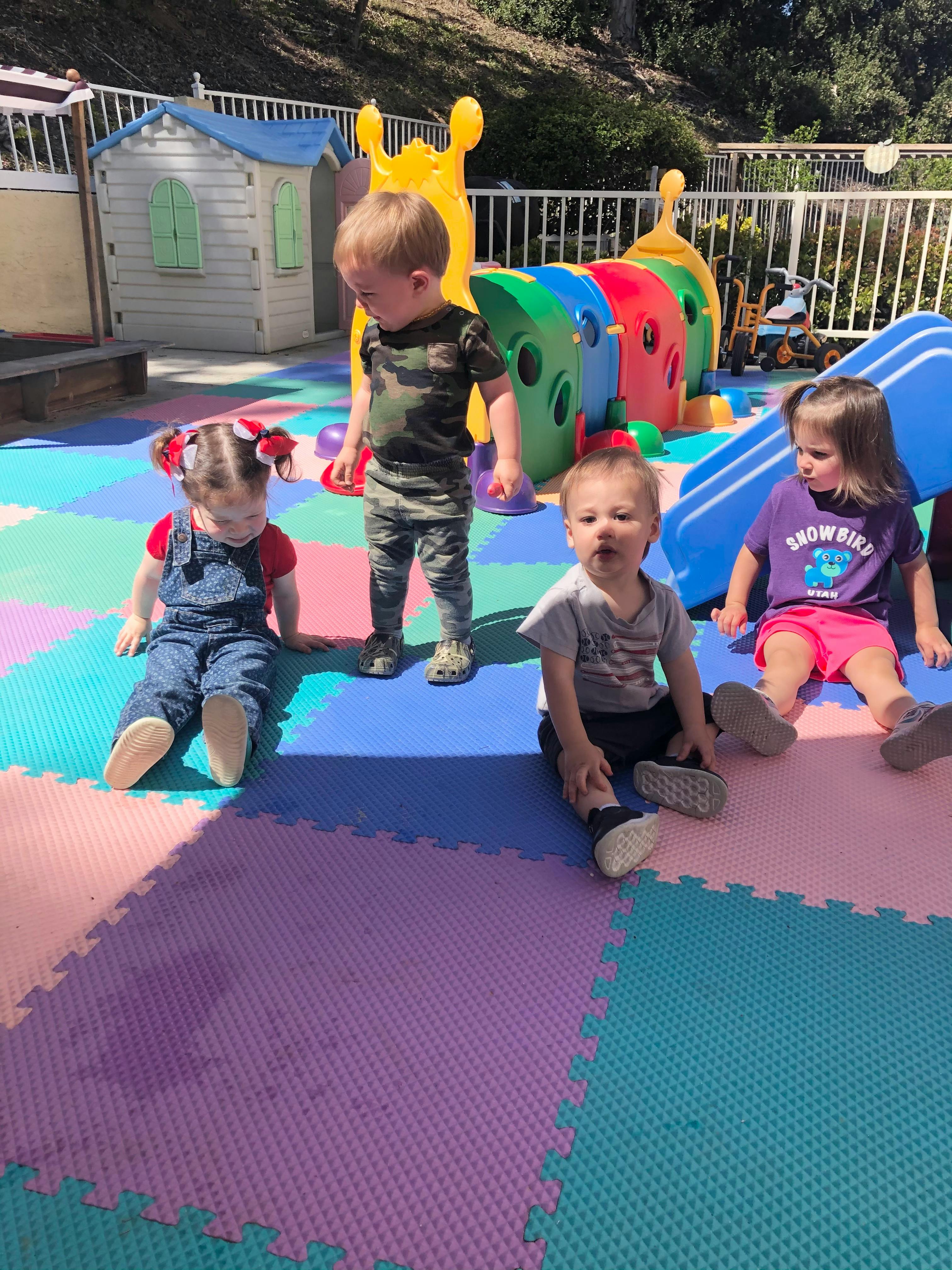 Four children on a colorful playground mat with play structures