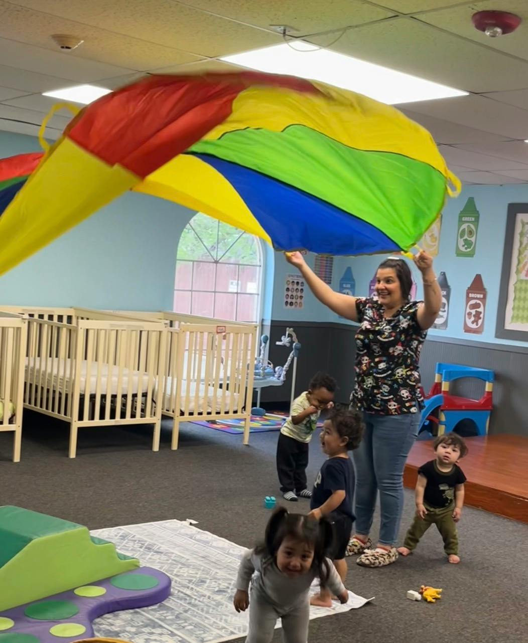 Adult and several children playing with a colorful parachute in a childcare room