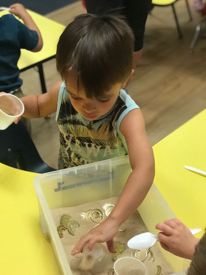 Child playing with sand and objects in a clear bin