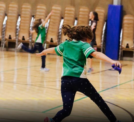 Child in green shirt playing on a gym floor