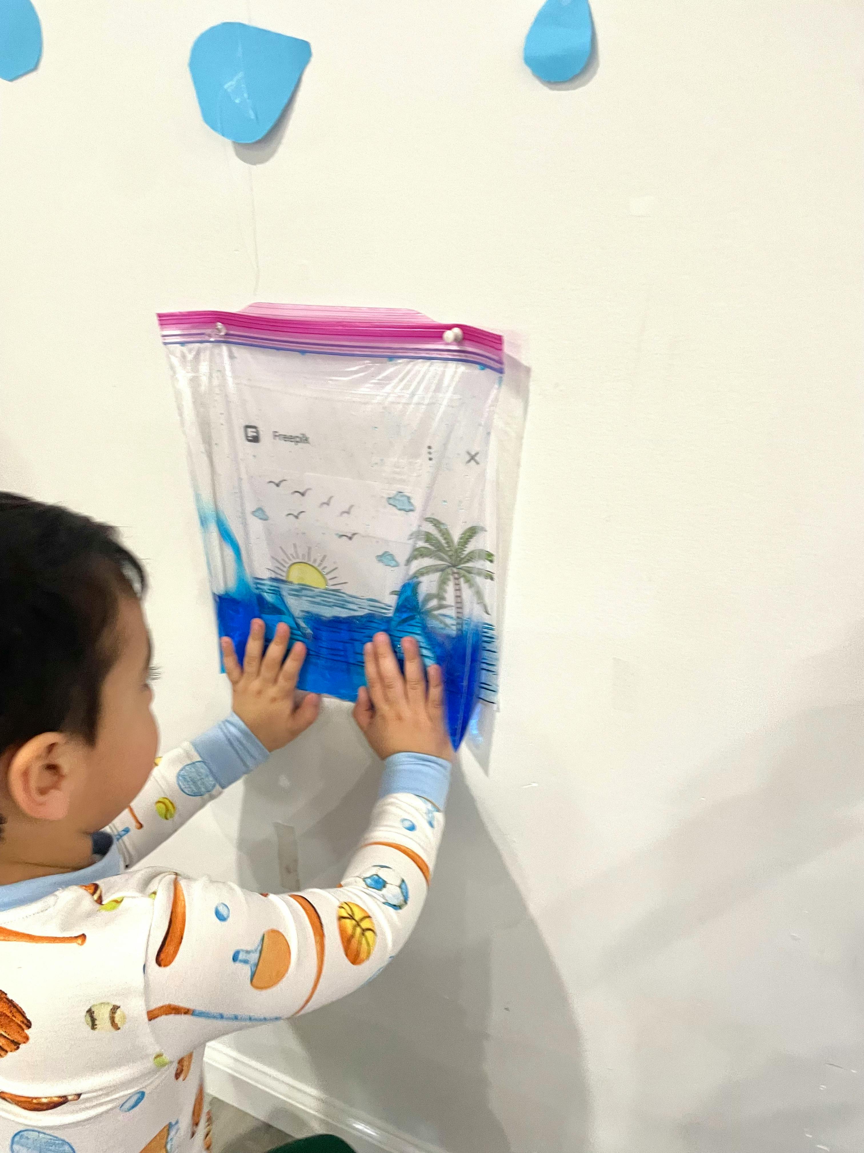 Child pressing hands on a clear bag filled with blue liquid attached to a wall