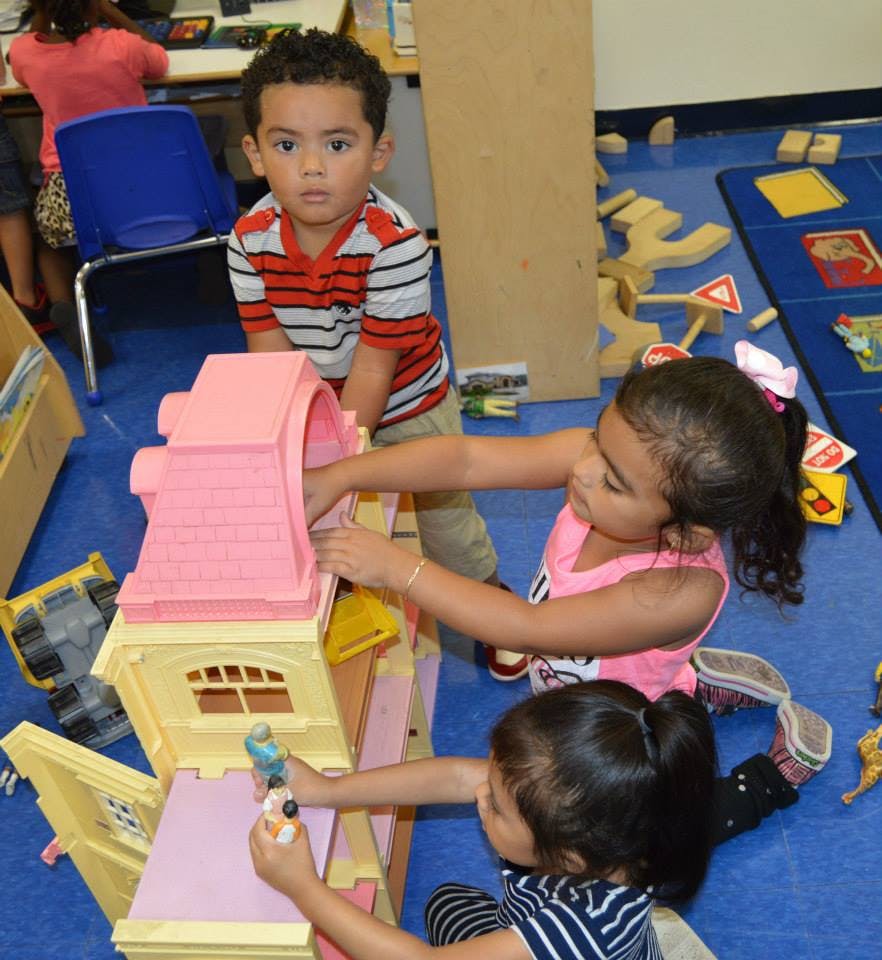 Three children playing with a dollhouse