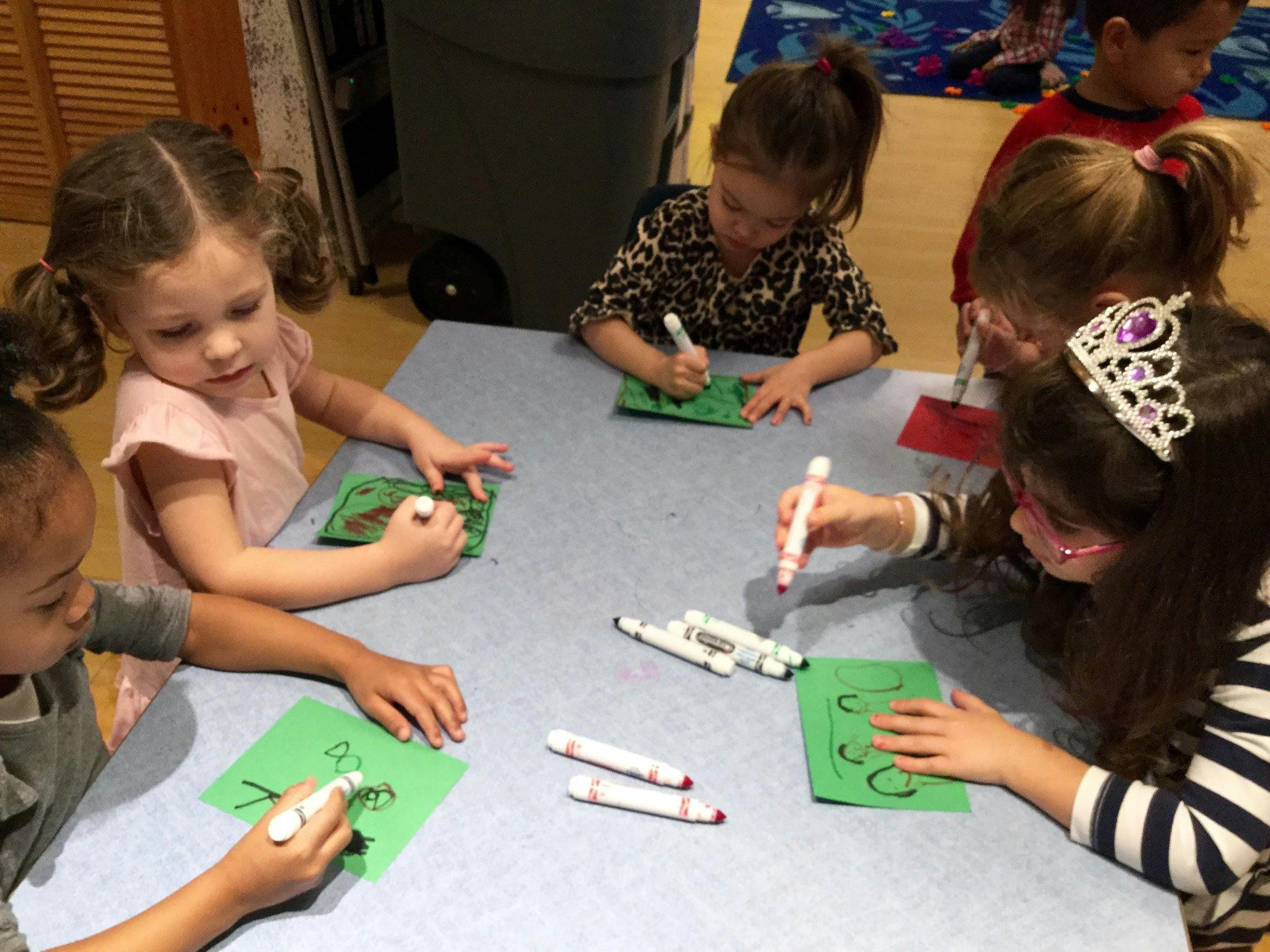 Children drawing on green paper at a table