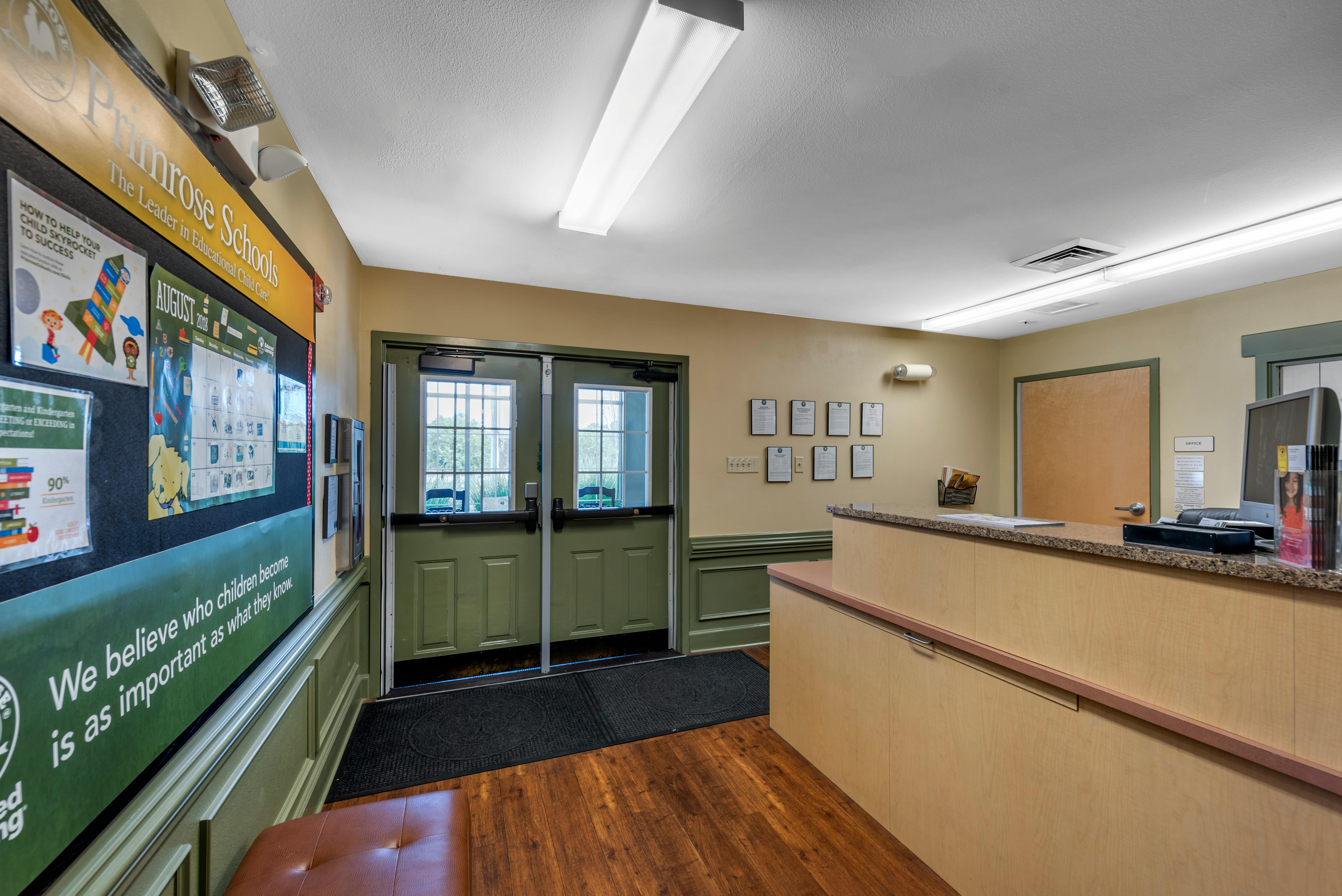 Lobby with a front desk, entrance doors, and a bulletin board with school information