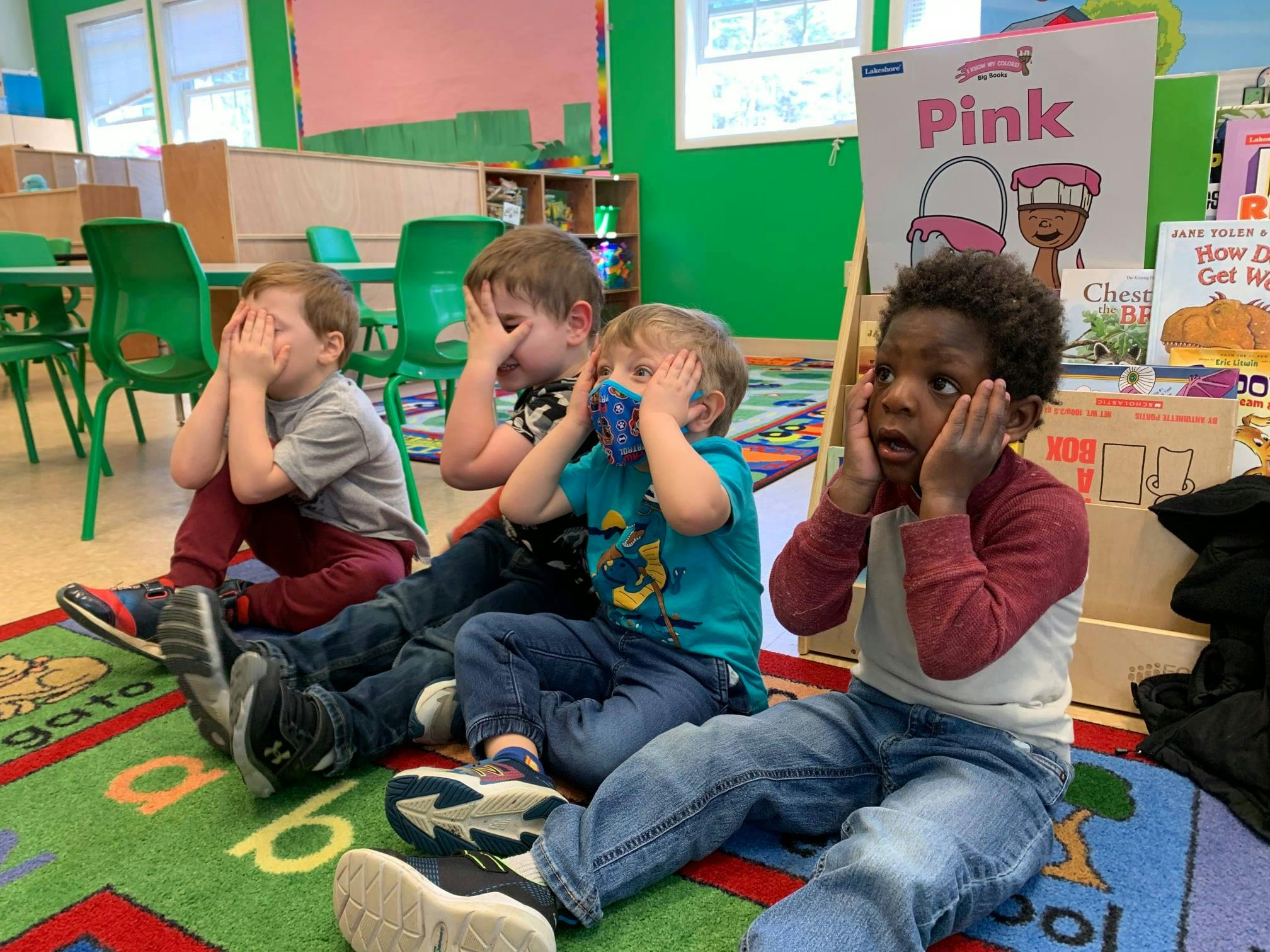 Four children covering their faces in a classroom