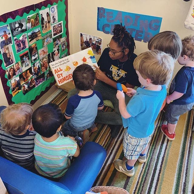 Person reading a book to several children in a classroom