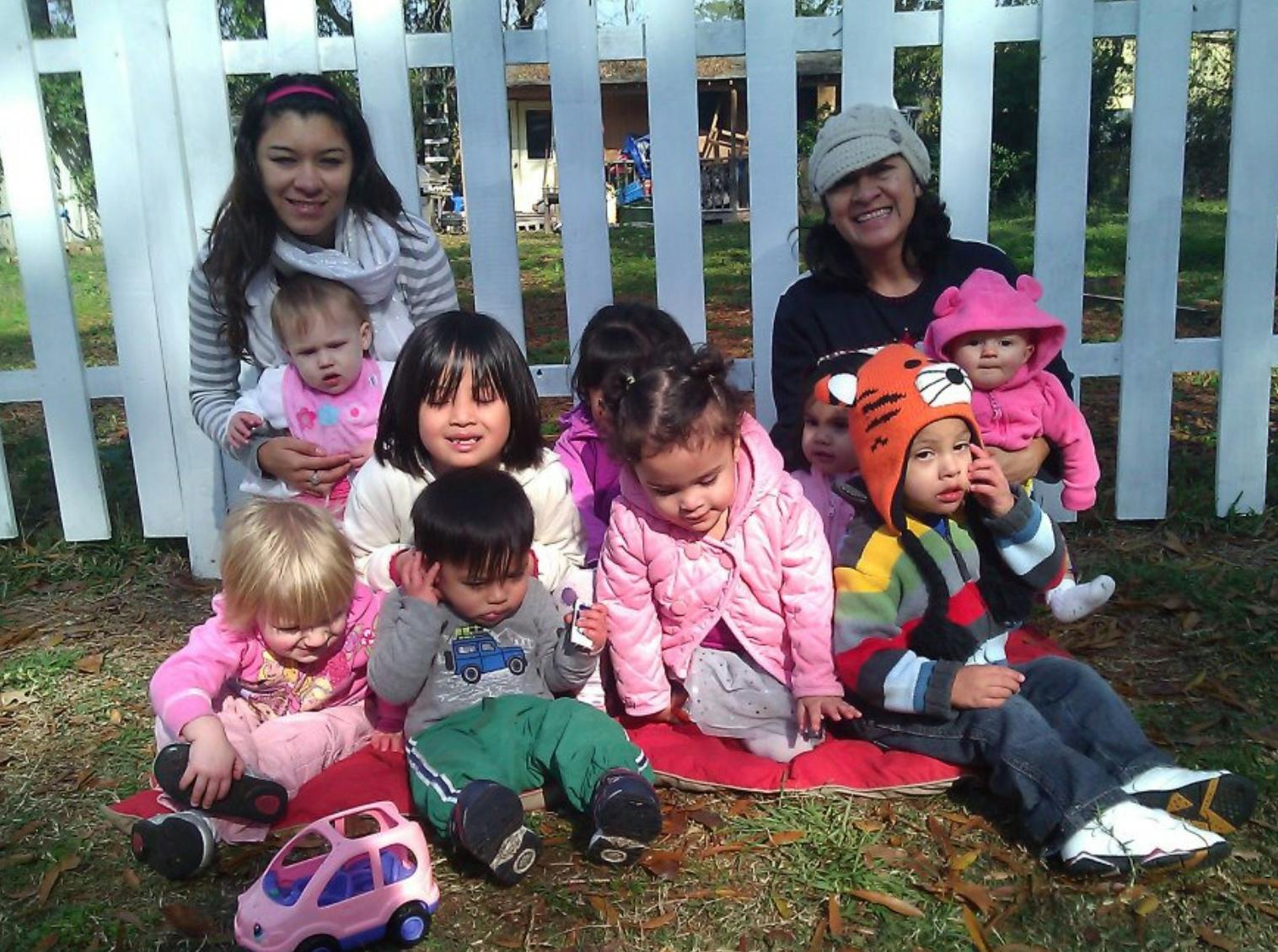 Two people with a group of children and babies sitting on the ground outdoors