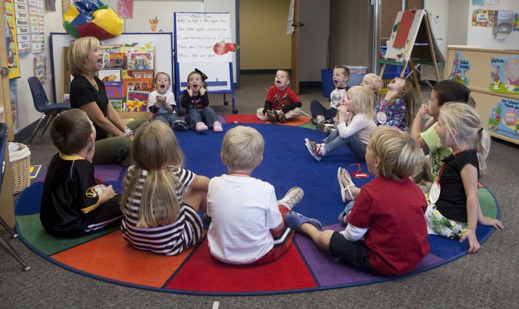 Adult and children sitting in a circle on a colorful rug in a classroom