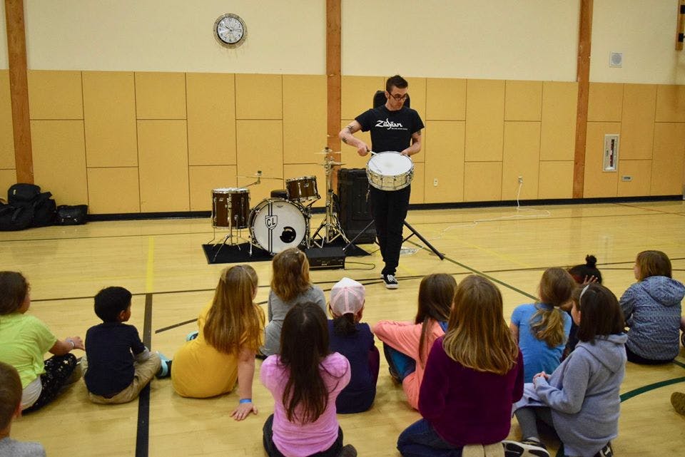 Person playing a drum for a group of children sitting on the floor