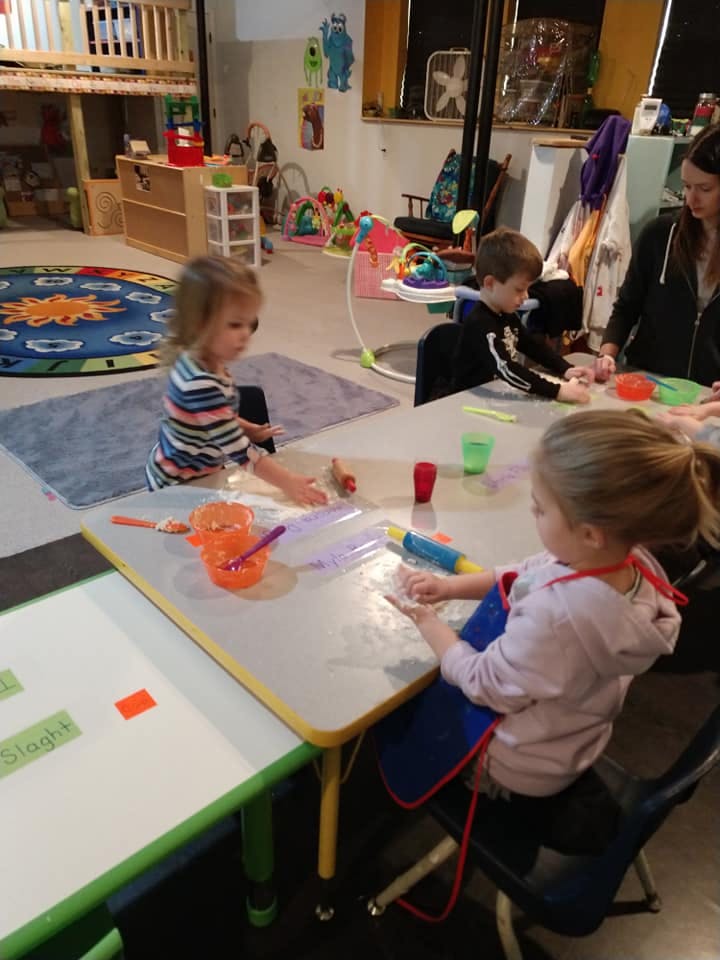 Children and an adult at tables in a room with toys