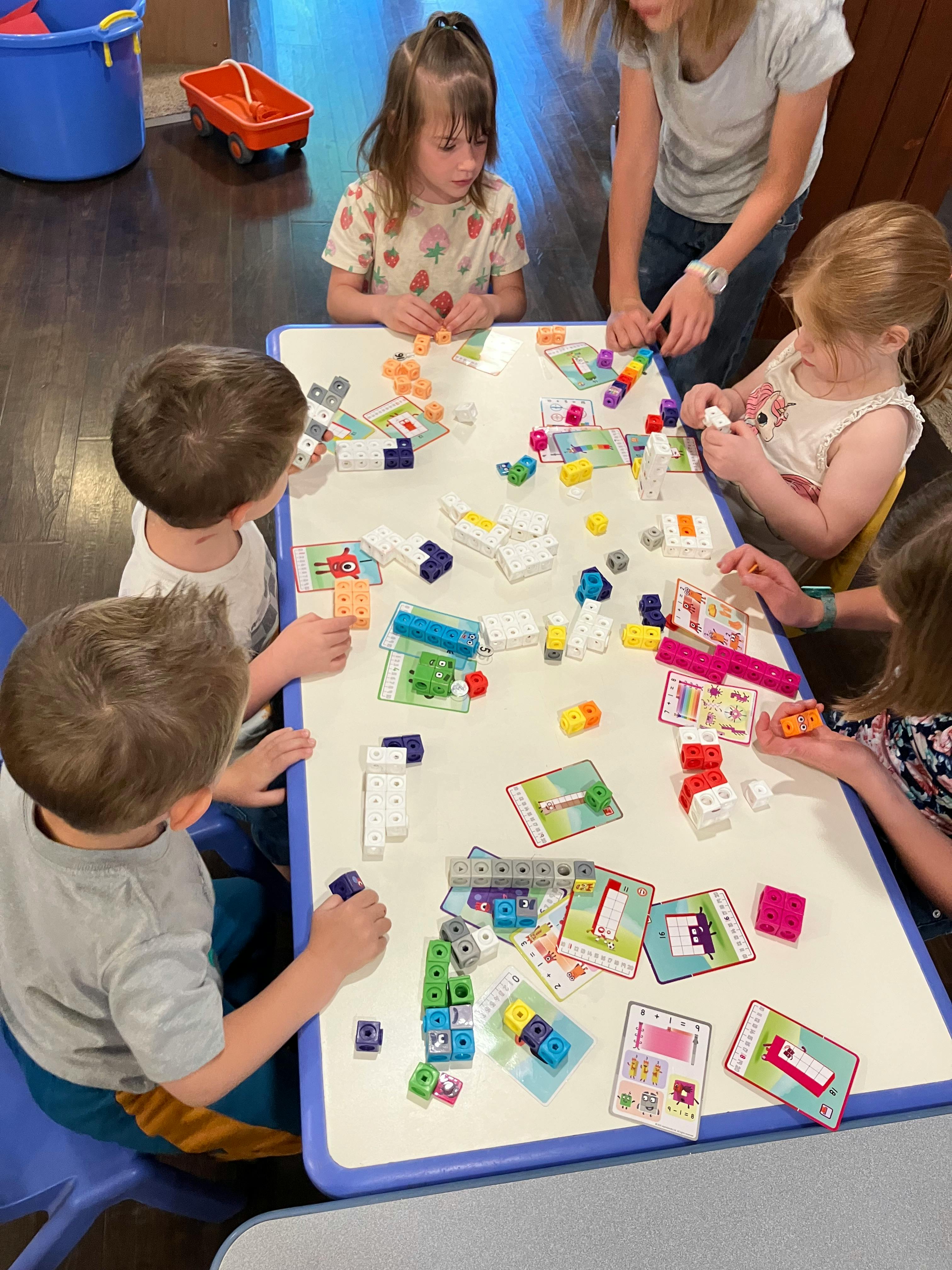 Adult and children playing with colorful blocks and cards at a table