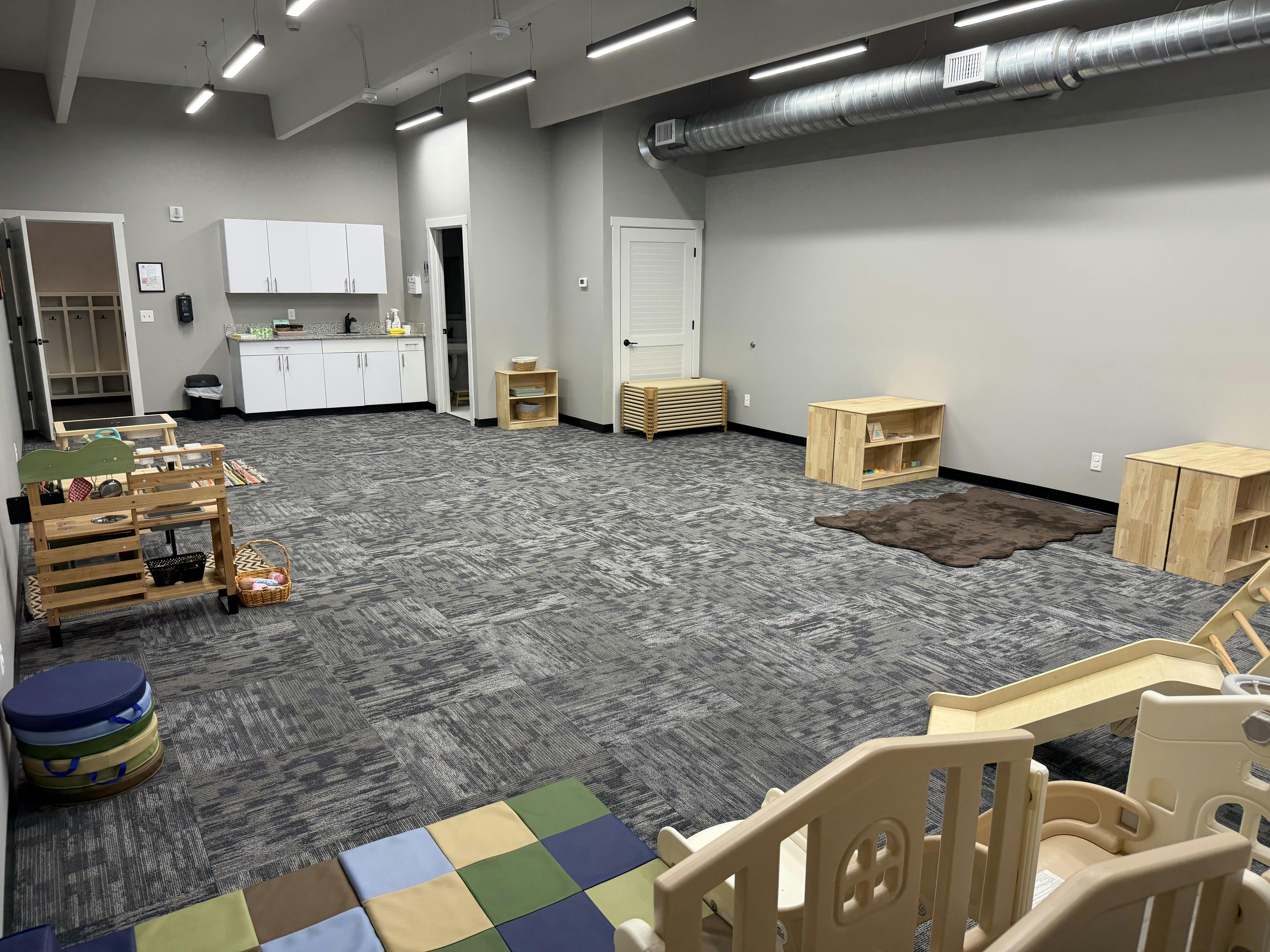 Spacious childcare room with wooden play equipment and area rugs