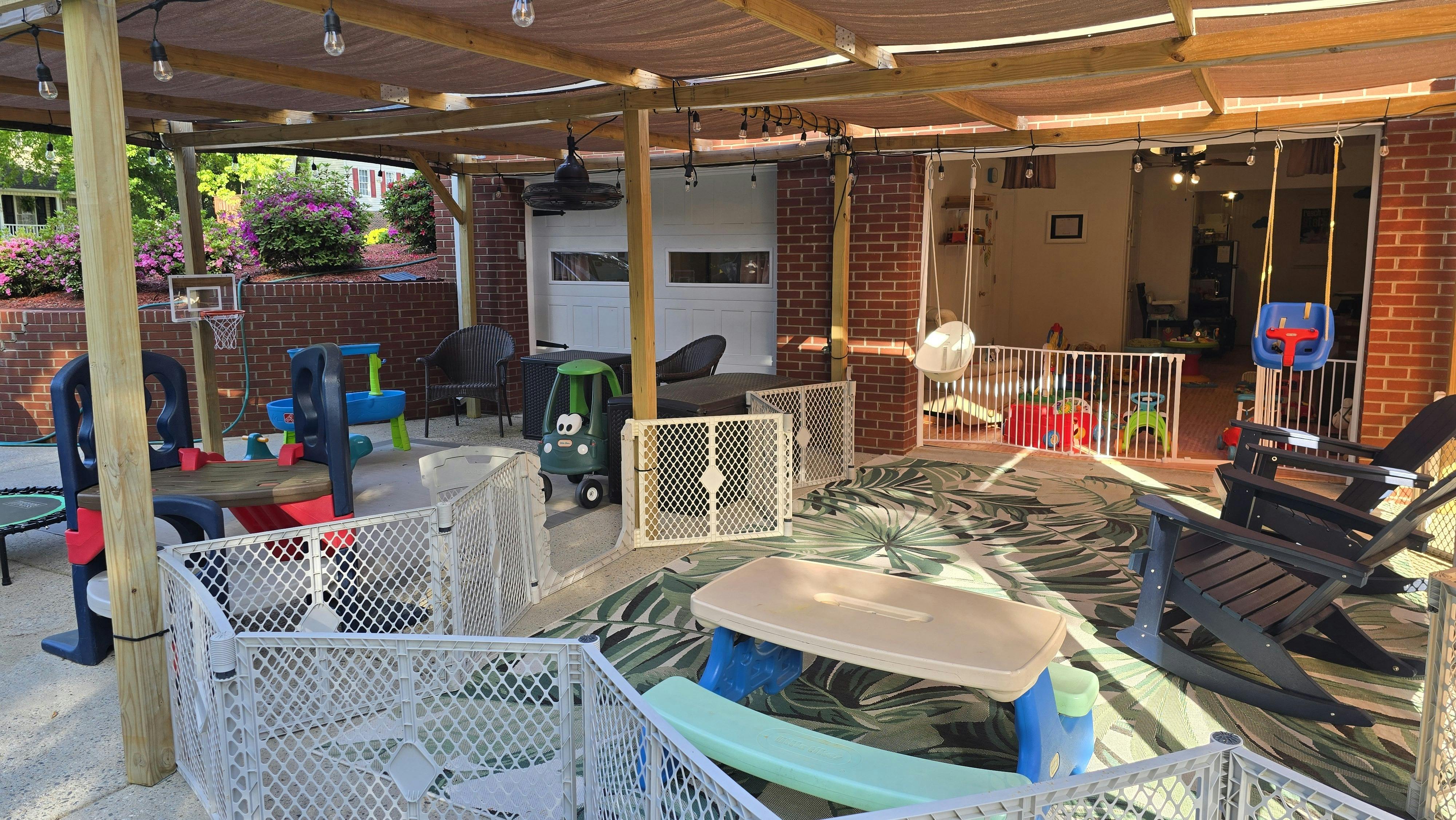 An outdoor patio play area with child gates, toys, and adult chairs