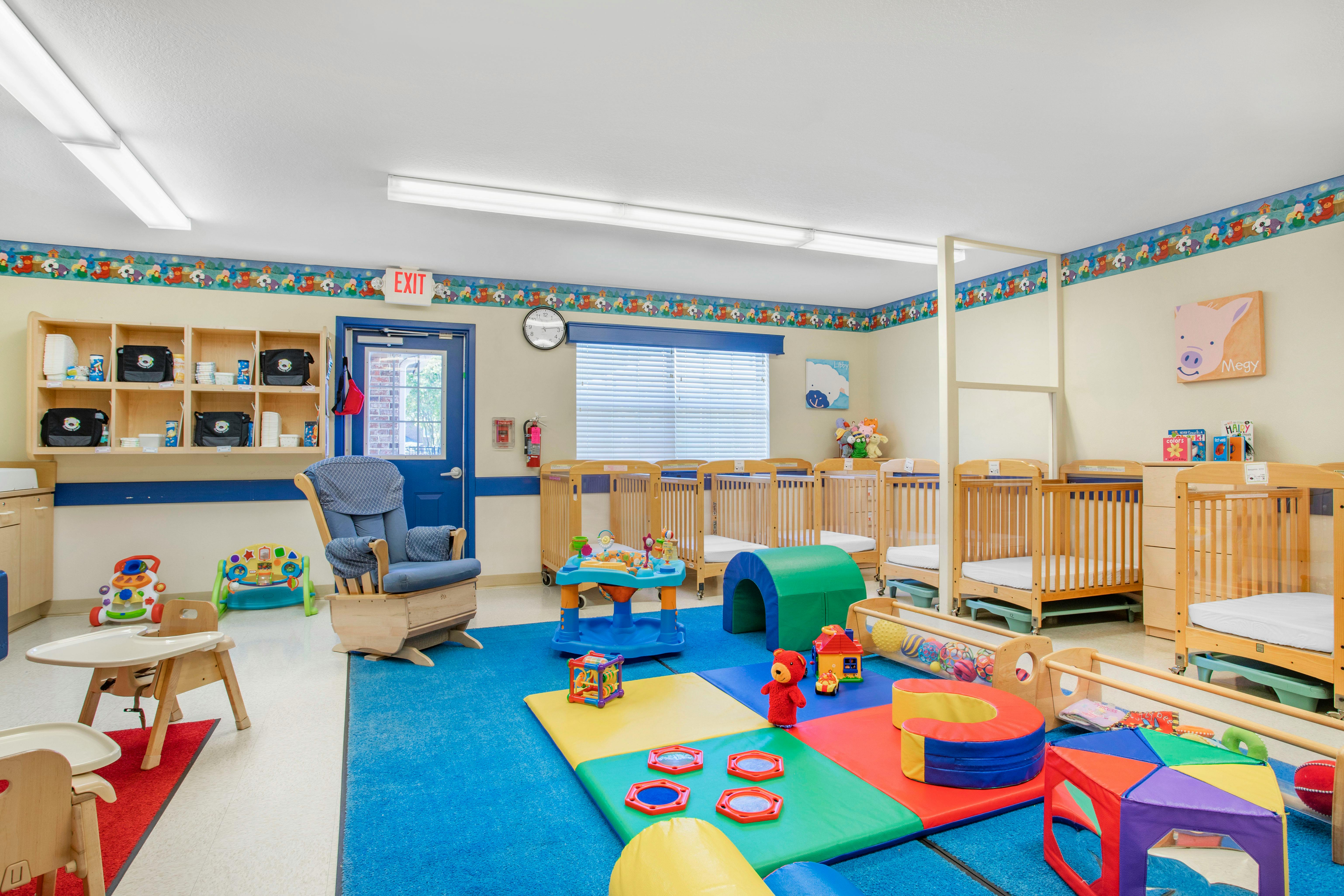 A colorful childcare room with cribs, play mats, and a rocking chair