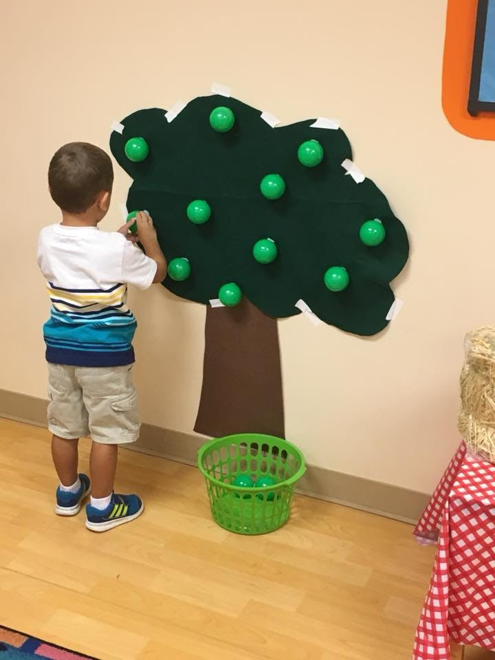 Child placing a green ball on a felt tree cutout on a wall