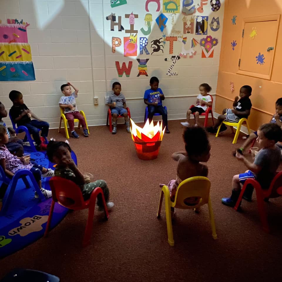 Children sitting in a circle around a faux campfire in a classroom